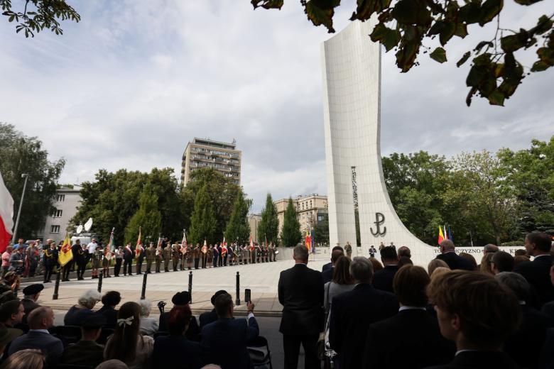 Grupa osób stoi przy Pomniku Armii Krajowej i Polskiego Państwa Podziemnego