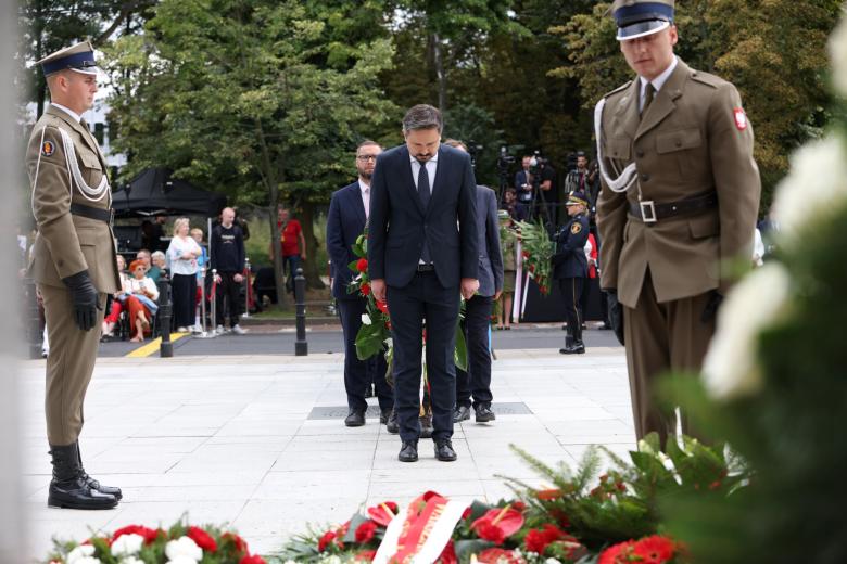 RPO Marcin Wiącek stoi pochylony, przed nim leży wieniec, obok stoją mężczyźni w mundurach wojskowych