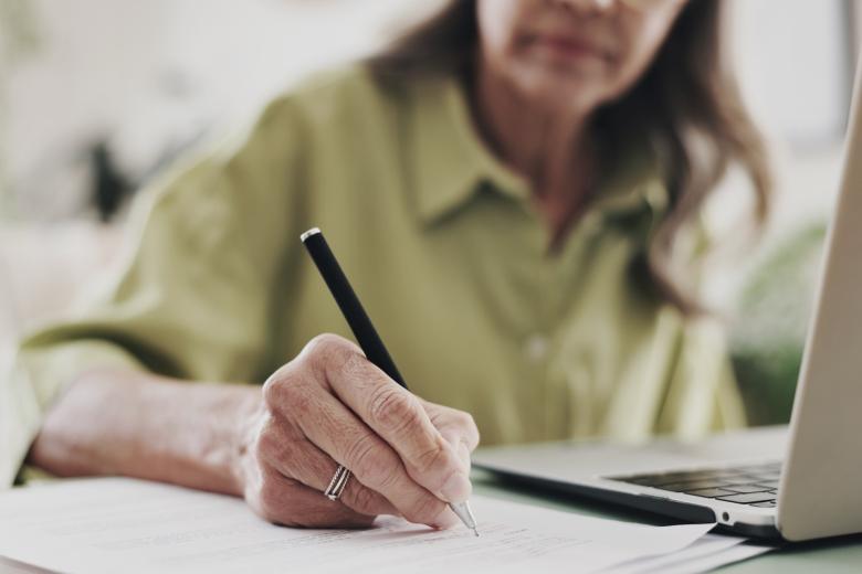 starsza osoba siedzi za stołem i pisze na papierze