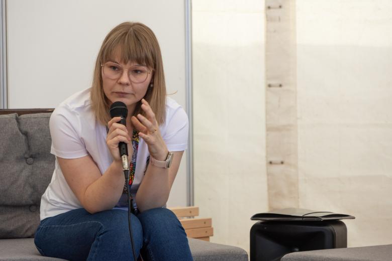 Kobieta ubrana w biały t-shirt i jeansy siedzi i trzyma w ręku mikrofon