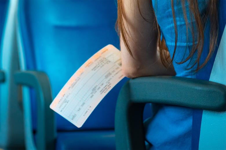 Siedząca w fotelu w wagonie bezprzedziałowym osoba trzyma w dłoni bilet pociągowy