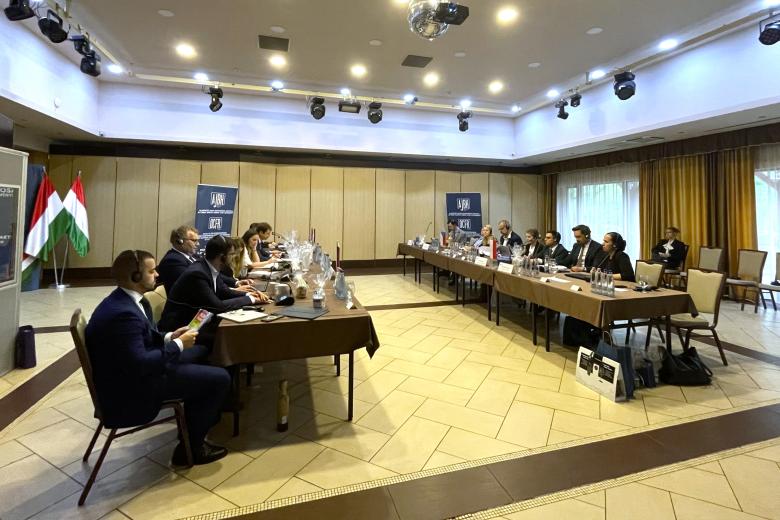 Kilkanaście osób siedzi po dwóch stronach stołów w sali konferencyjnej