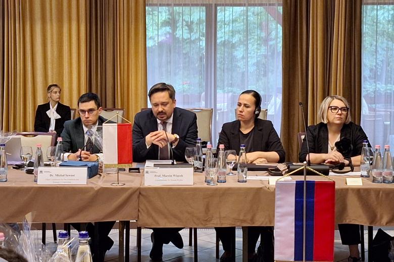 Pięć osób siedzi przy stole na którym stoi mała biało-czerwona flaga