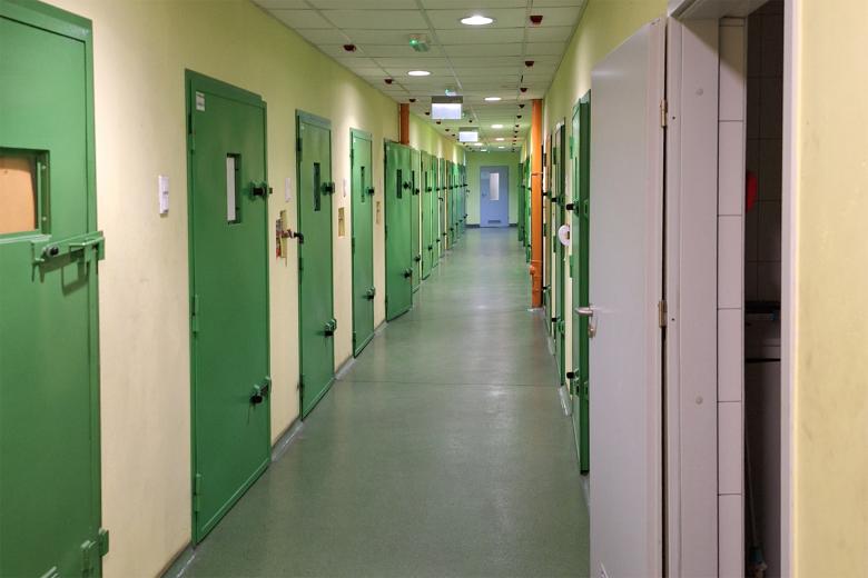 Zdjęcie przedstawiające szereg wzmacnianych, stalowych drzwi w długim korytarzu. W drzwiach są niewielkie okienka.