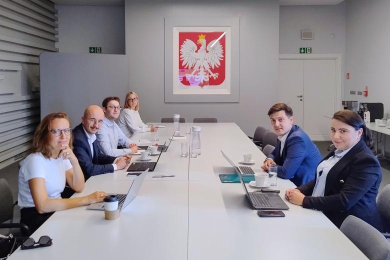 Sześć osób siedzi przy stole konferencyjnym i uśmiecha się, pozując do zdjęcia