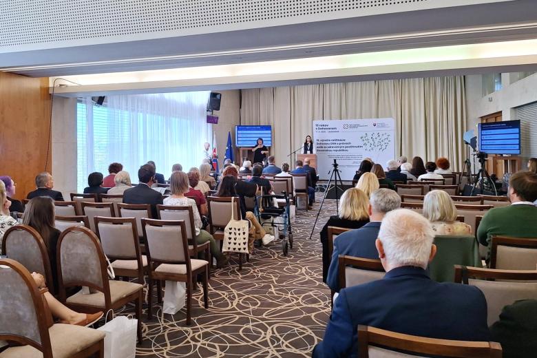 Kilkadziesiąt osób na sali konferencyjnej słucha wystąpienia osoby mówiącej za mównicą