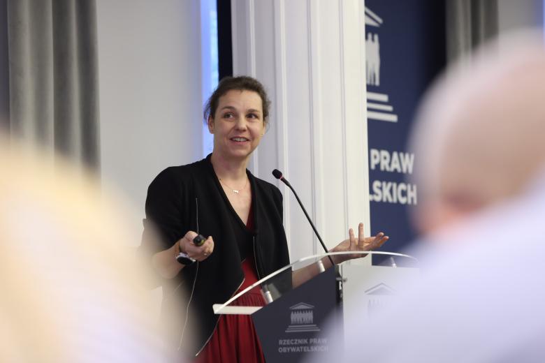 Osoba przemawia za mównicą w sali konferencyjnej