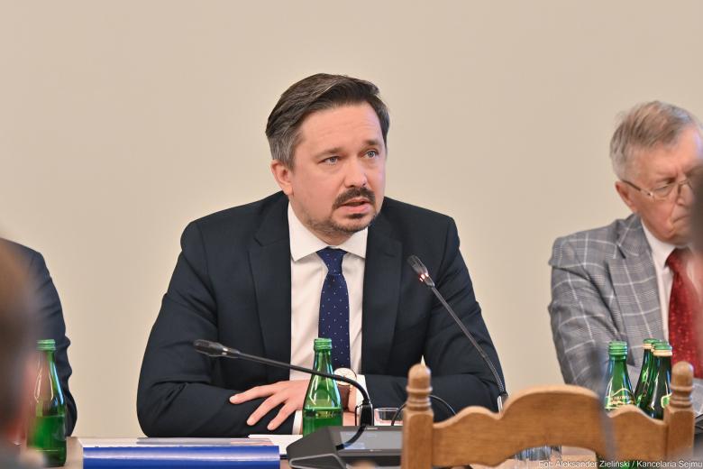 RPO Marcin Wiącek wypowiada się do mikrofonu siedząc przy stole w sali konferencyjnej