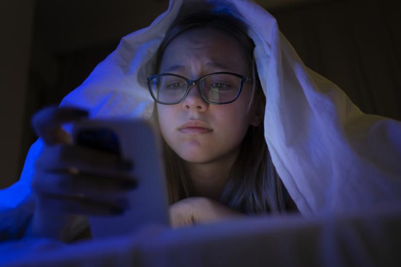 młoda osoba patrzy z niechęcia na smartfon  na ciemnym tle
