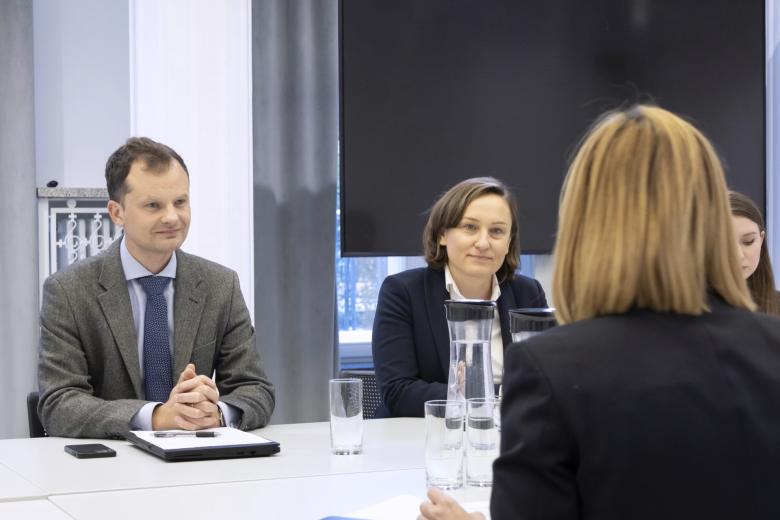 Dwie osoby siedzące za stołem z uwagą słuchają osoby, która siedzi na przeciwko