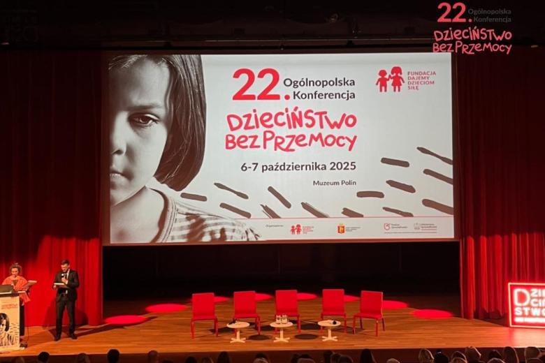 Aula wykładowa z wyświetlonym na ekranie wizerunkiem twarzy smutnego dziecka i dużym napisem "22. Ogólnopolska Konferencja Dzieciństwo bez przemocy"