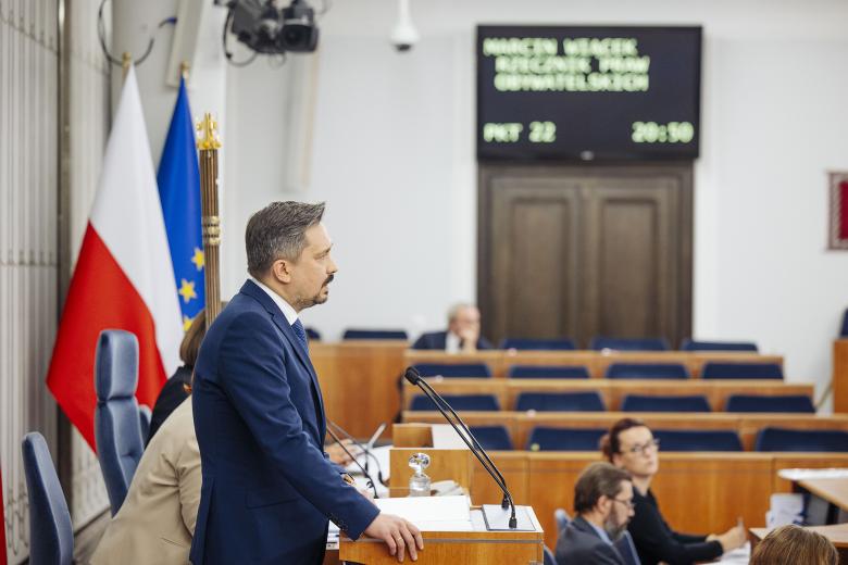 RPO Marcin Wiącek wypowiada się stojąc przy mównicy w sali posiedzeń Senatu.