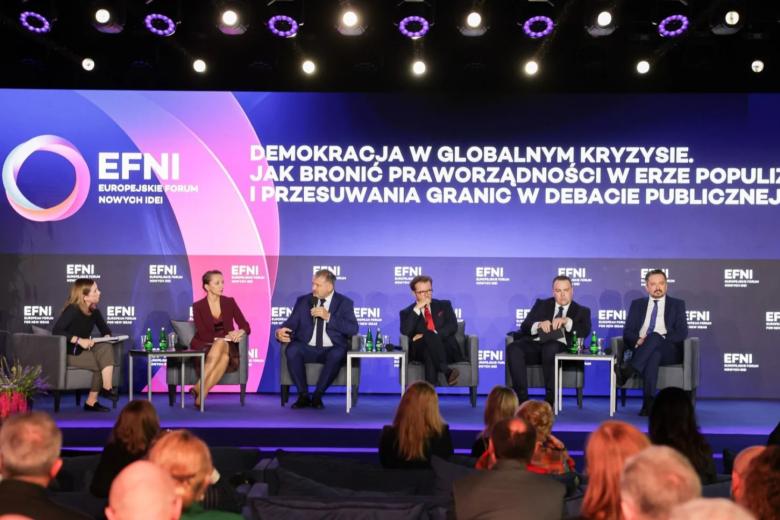Sześć osób siedzi na scenie, w tle na dużej planszy napis "Europejskie Forum Nowej Idei. Demokracja w globalnym kryzysie. Jak bronić praworządności w erze populizmu i przesuwania granic w debacie publicznej?"