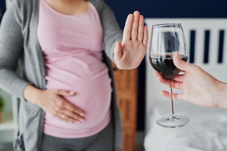 Kobieta w ciąży gestem dłoni odmawia podawanego jej kieliszka z winem