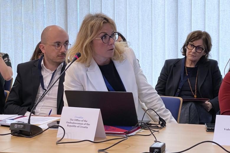Trzy osoby siedzą na fotelach przy stole na sali konferencyjnej