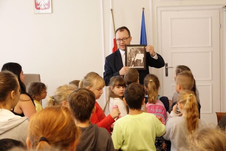 zdjęcie: mężczyzna sto i i pokazuje zdjęcie w ramce otaczającym go dzieciom 