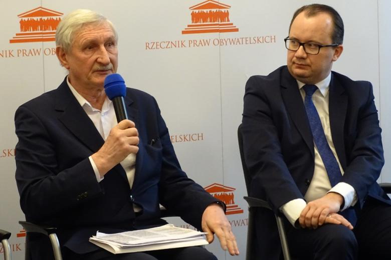 zdjęcie: dwaj mężczyźni siedzą na krzesłach, jeden z nich mówi do mikrofonu