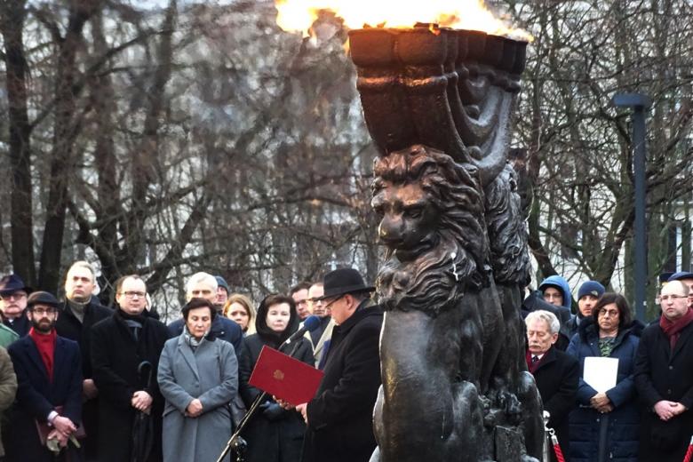 zdjęcie: na pierwszym planie fragment pomnika, za nim widoczna grupa stojących osób