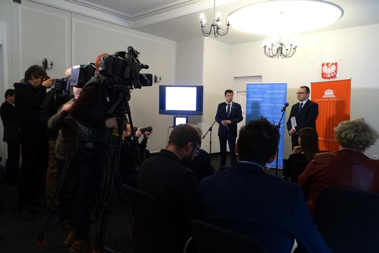 zdjęcie: na pierwszym planie stoją kamery, obok nich dziennikarze, przed nimi dwóch mężczyzn