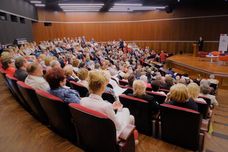 zdjęcie: na scenie przy mównicy stoi mężczyzna przed nim siedzi ok. 300 osób