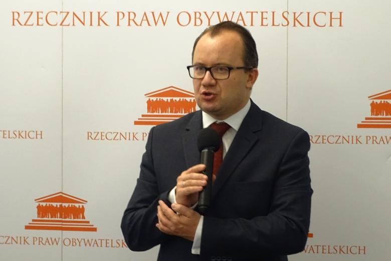 zdjęcie: mężczyzna w garniturze stoi na tle biało-pomarańczowego baneru