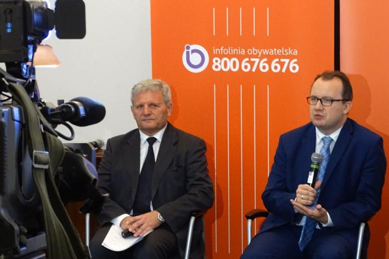 zdjęcie: na pierwszym planie widać fragment kamery, w tle siedzi dwóch mężczyzn w garniturach