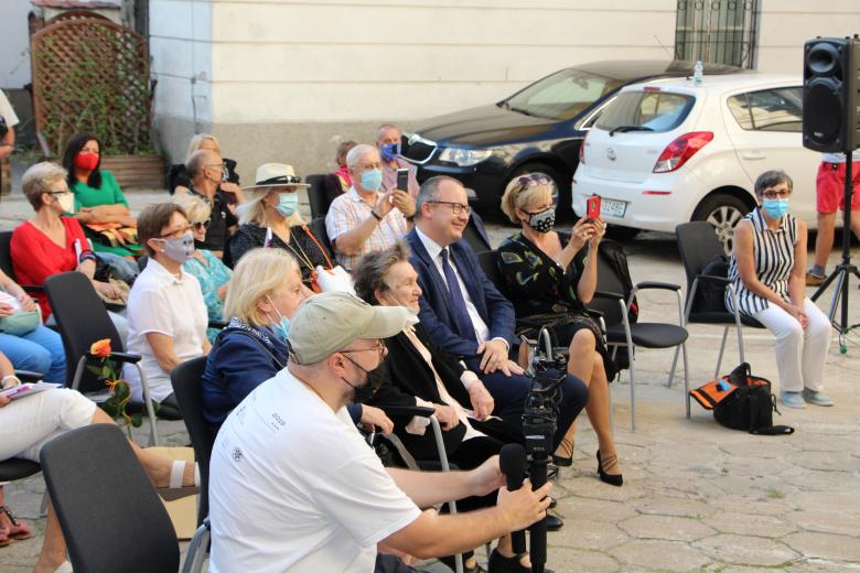 tłum ludzi w kolorowych maseczkach i ubraniach siedzi na krzesłach