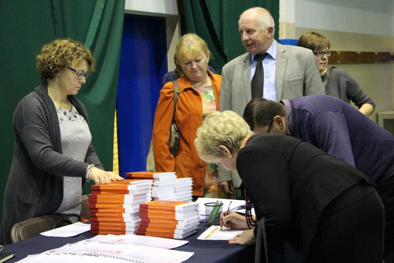 zdjęcie: kilka osób stoi przy stoliku na którym leżą publikacje