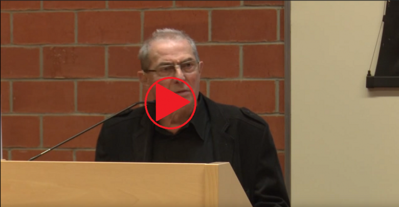 Szpakowaty mężczyzna na mównicy, znal "play"