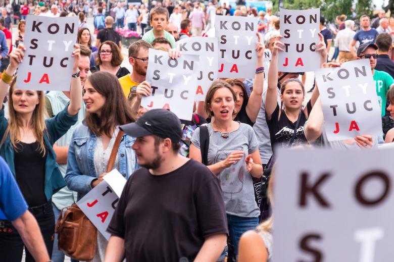 Protestujący ludzie trzymający plakat KonsTYtucJA