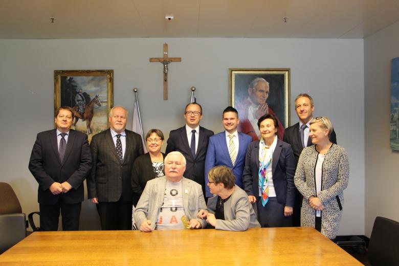 Zdjęcie grupowe. Mężczyzna w koszulce z napisem KonsTYtucJA otoczony przez gości. W tle: krzyż, portret papieża Jana Pawła II i portret marszałka Piłsudskiego