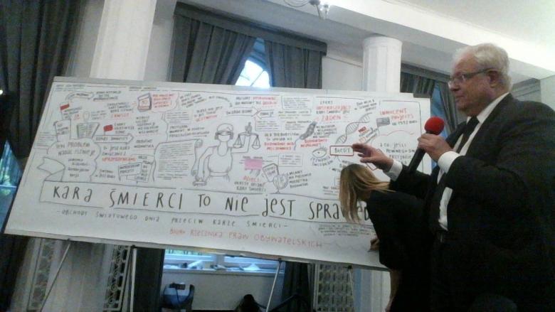 Mężczyzna rzemawia na tle wielkiego rysunku