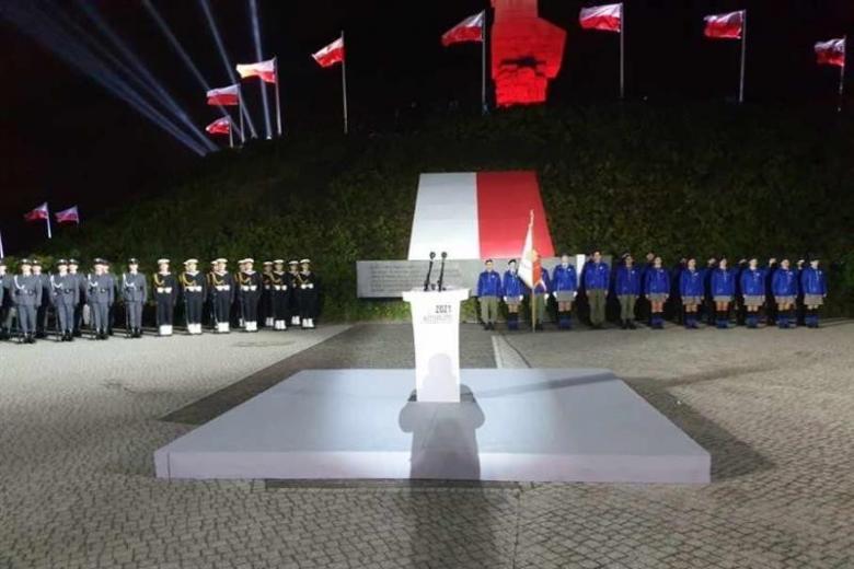 przygotowania do uroczystości, pusta mównica, w tle w dwuszeregu wojsko i harcerze oraz polskie flagi