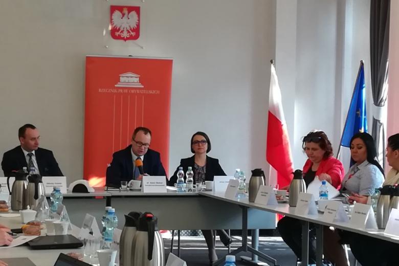 Kobiety i mężczyźnie przy czworokątnym stole, z tyłu banner RPO oraz flagi Polski I UE