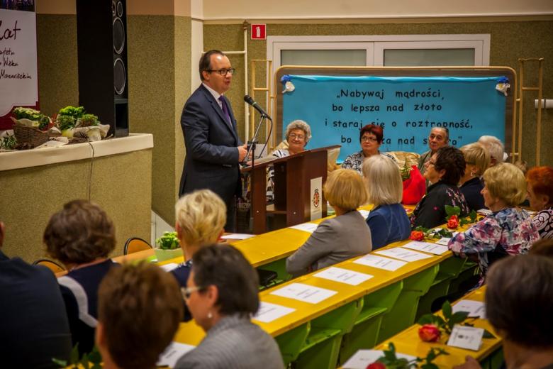 zdjęcie: mężczyzna w garniturze stoi i przemawia do kilkudziesięciu osób