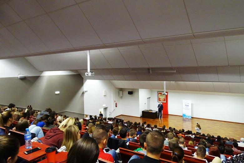 Aula wykładowa pełna słuchaczy, mezczyzna na scenie