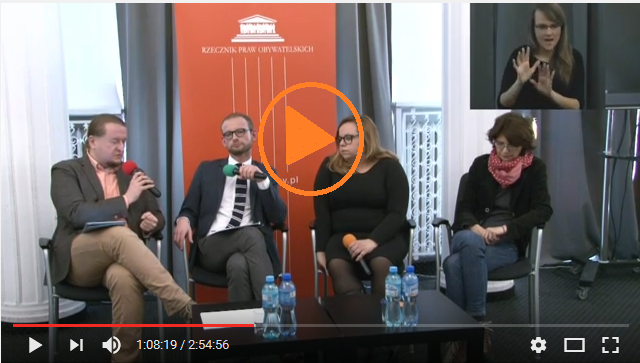 zdjęcie: cztery sobowy siedzą przy małym stoliku, mężczyzna po lewej mówi do mikrofonu