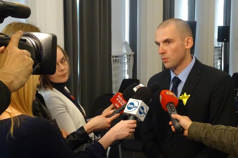 Mężczyzna z żółtym żonkilem rozmawia z dziennikarzami