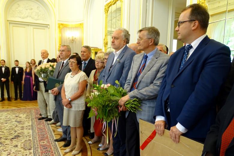 zdjęcie: kilkanaście osób stoi, niektorzy z nich mają bukiety kwiatów