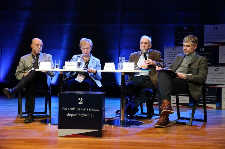 Paneliści na scenie. Przed nimi sześcian z nazwą panelu