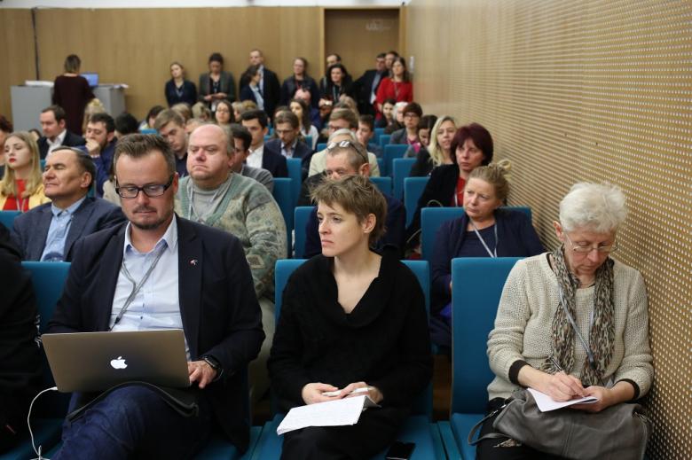 Sala pełna ludzi, na pierwszym planie mężczyzna notuje na laptopie