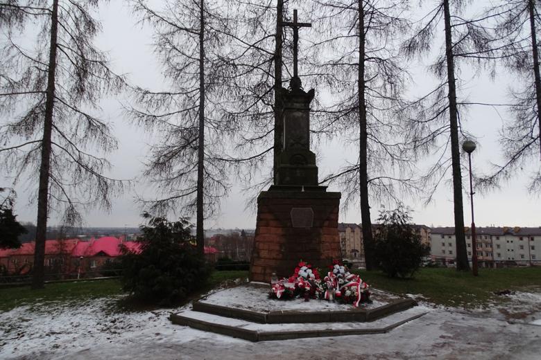 Krzyż koło kościoła z wieńcami z biało-czerwonymi wstęgamiu