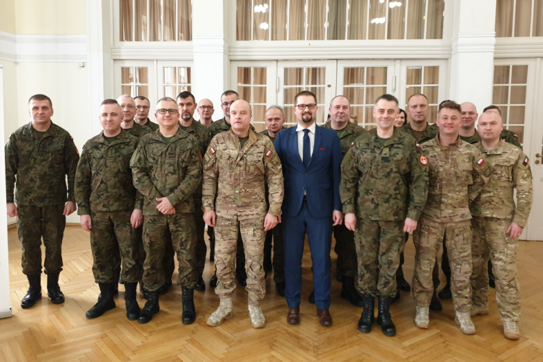 Zdjęcie grupowe - mężczyźni w polowych mundurach wojskowych i mężczyzna w garniturze