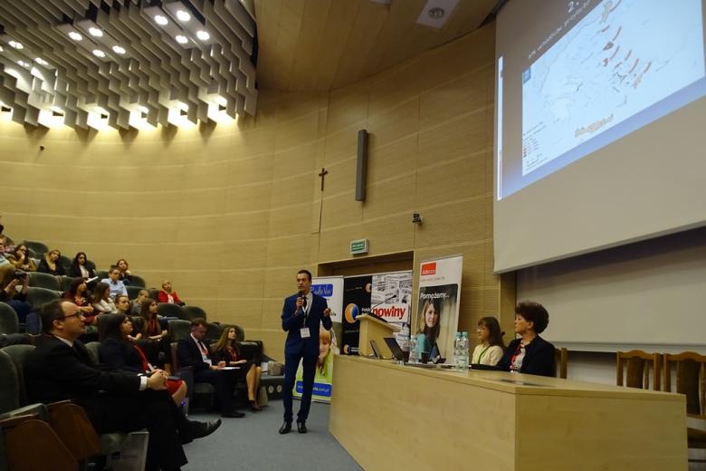 Zdjęcie: młody mężczyzna przedstawia prezentacje. Na ekranie mapa Polski ze strzałkami ze wschodu