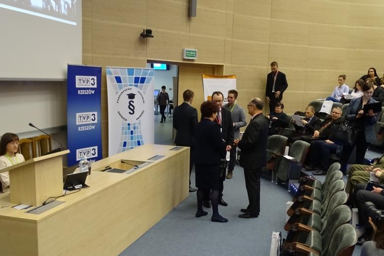 Zdjęcie: ludzie gromadzą się w dużej nowoczesnej sali wykładowej o amfiteatralnym układzie