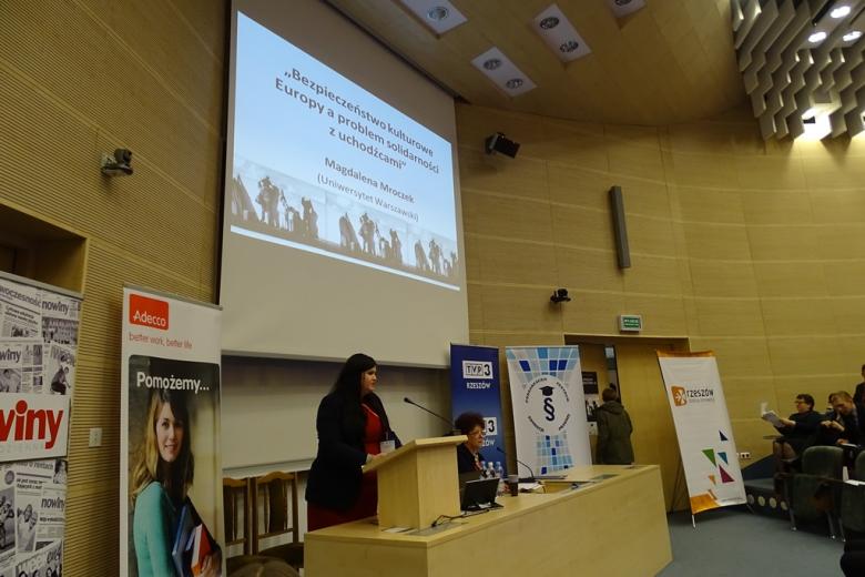 Zdjęcie: młoda kobieta w czerwonej sukni i ciemnym żakiecie na mównicy