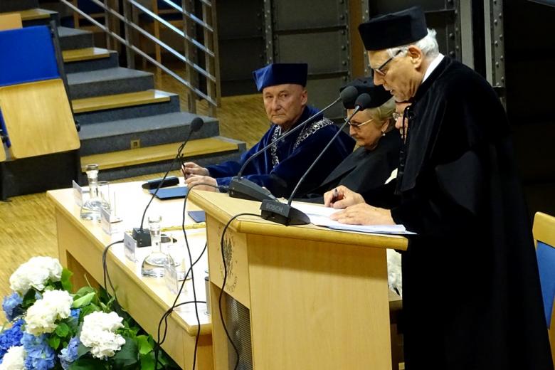 zdjęcie: mężczyzna w tudze stoi przy mównicy, po jecgo lewej stronie widać osoby siedzące przy stole konferencyjnym