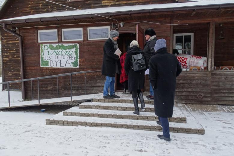 Zima. Ludzie wchodzą do drewnianego budynku na wsi