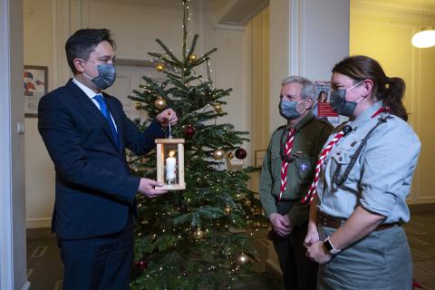 Rzecznik trzymający znicz rozmawia z dwoma harcerzami stojąc przy świątecznej choince