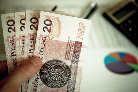 cztery banknoty dwudziestozłotowe trzymane w dłoni na tle dokumentów i kalkulatora